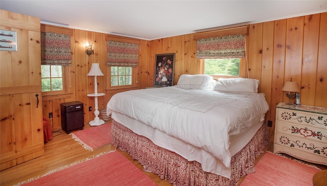 bedroom with multiple windows, light wood finished floors, and wooden walls