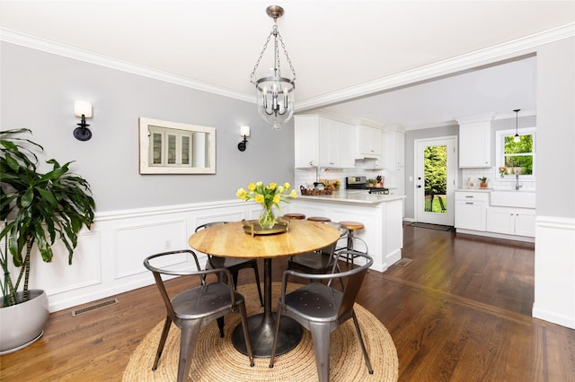 dining space with dark wood-style flooring, ornamental molding, wainscoting, and a chandelier