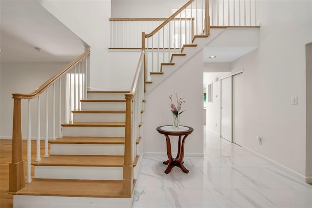 stairs featuring marble finish flooring, baseboards, and a high ceiling