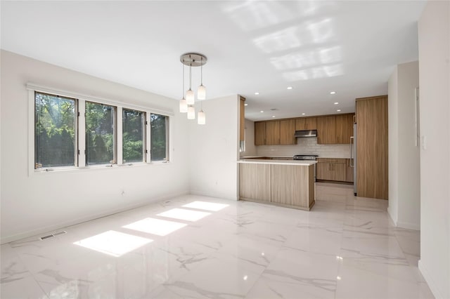 kitchen featuring under cabinet range hood, brown cabinetry, baseboards, tasteful backsplash, and light marble finish flooring