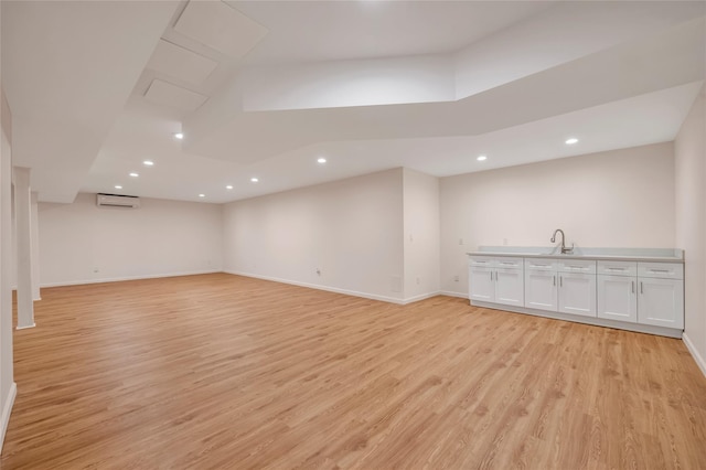 below grade area with a wall mounted air conditioner, light wood-type flooring, recessed lighting, baseboards, and a sink