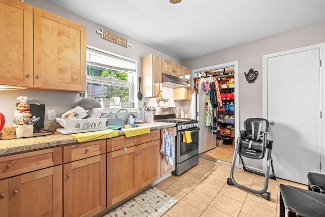 kitchen with gas stove, a sink, under cabinet range hood, light tile patterned floors, and decorative backsplash