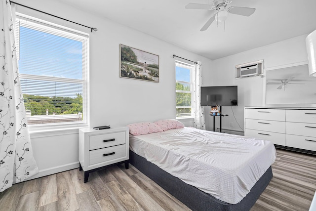 bedroom featuring wood finished floors, baseboards, a wall unit AC, and a ceiling fan
