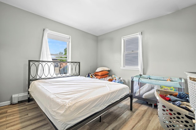 bedroom featuring wood finished floors, a baseboard heating unit, and baseboards