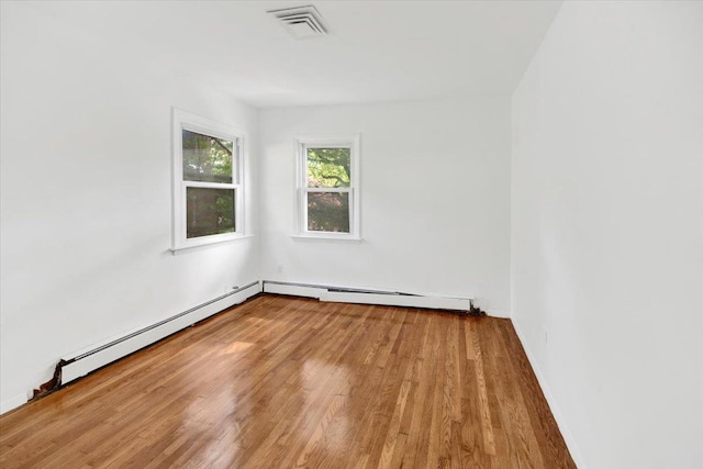 unfurnished room with wood finished floors, baseboard heating, and baseboards
