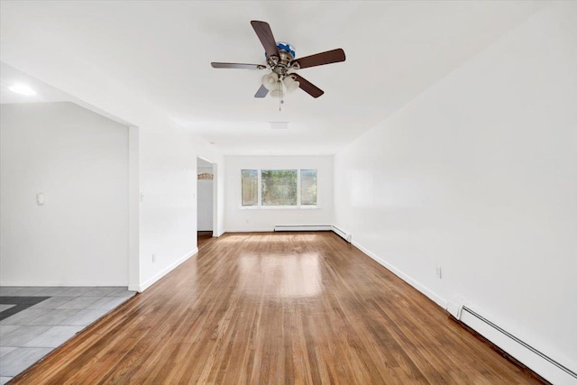 empty room with baseboard heating, a baseboard heating unit, a ceiling fan, wood finished floors, and baseboards
