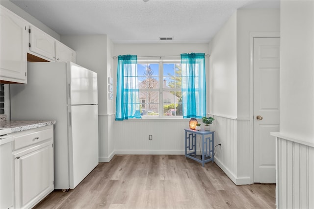 37 Spruce St, Pawling, NY 12564 - kitchen with light wood-style floors, freestanding refrigerator, light countertops, a wainscoted wall, and white cabinetry