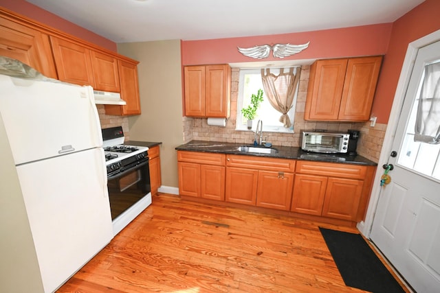 kitchen with freestanding refrigerator, gas stove, under cabinet range hood, a sink, and tasteful backsplash