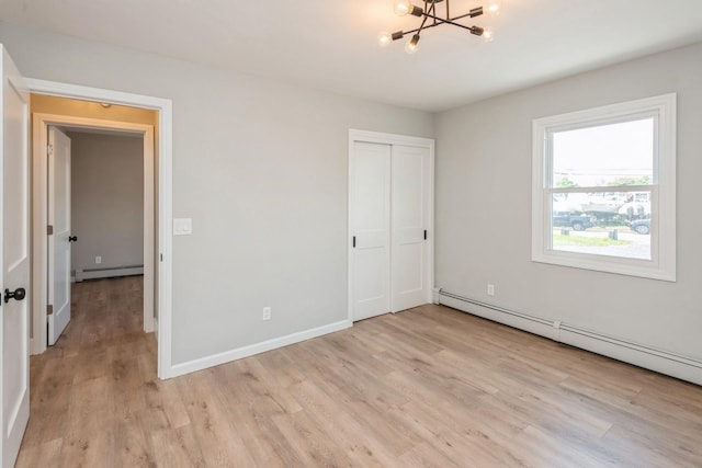 unfurnished bedroom featuring baseboard heating, light wood-type flooring, a chandelier, and a closet
