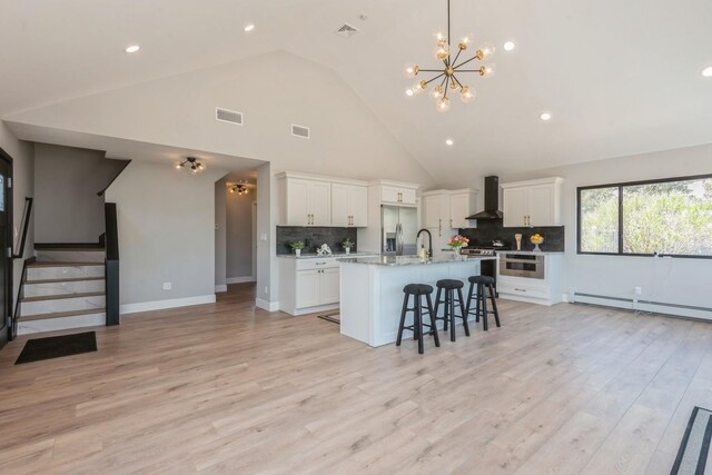 kitchen with wall chimney exhaust hood, appliances with stainless steel finishes, a sink, baseboard heating, and a kitchen bar