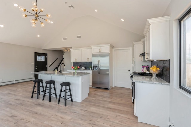 kitchen featuring appliances with stainless steel finishes, a baseboard heating unit, a kitchen breakfast bar, white cabinets, and a chandelier
