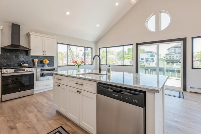kitchen featuring appliances with stainless steel finishes, wall chimney range hood, a sink, high vaulted ceiling, and light wood finished floors