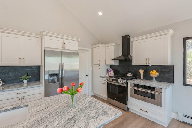 kitchen featuring appliances with stainless steel finishes, wall chimney exhaust hood, baseboard heating, white cabinetry, and tasteful backsplash