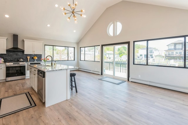 kitchen featuring wall chimney range hood, appliances with stainless steel finishes, a sink, high vaulted ceiling, and white cabinetry