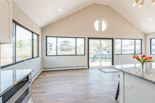 kitchen featuring high vaulted ceiling, light stone counters, light wood-style floors, a baseboard radiator, and a chandelier