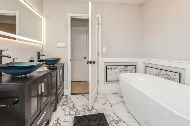 full bathroom with marble look tile flooring, a freestanding tub, and double vanity