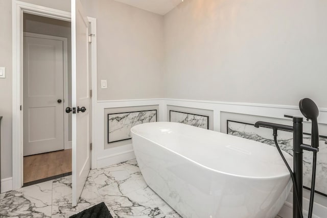 bathroom featuring marble look tiles, a wainscoted wall, and a soaking tub