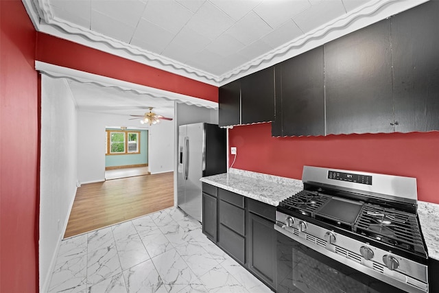 kitchen with appliances with stainless steel finishes, light marble finish flooring, dark cabinets, a ceiling fan, and baseboards