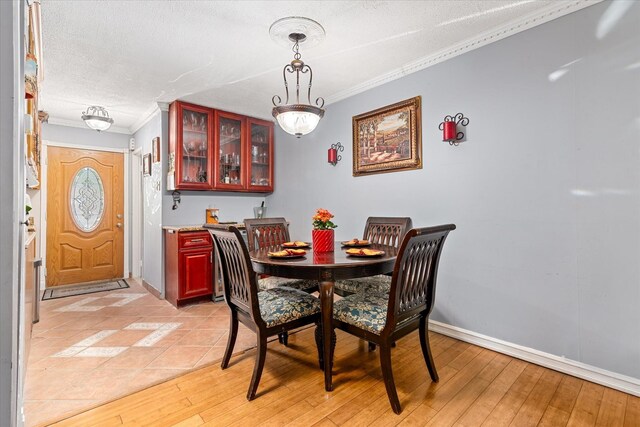 dining area featuring ornamental molding, a textured ceiling, light wood finished floors, and baseboards