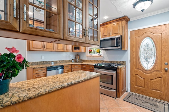 kitchen featuring stainless steel appliances, light stone countertops, light tile patterned floors, brown cabinets, and crown molding