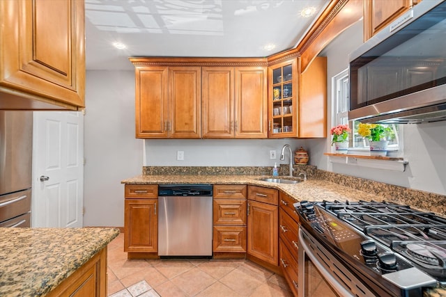 kitchen with stainless steel appliances, a sink, brown cabinets, light stone counters, and recessed lighting