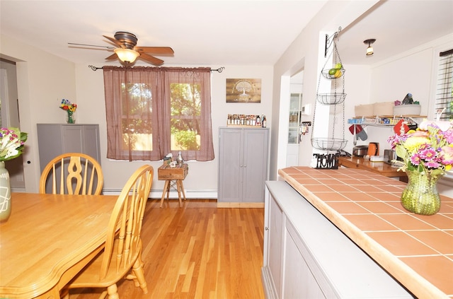 dining room with light wood-style flooring, ceiling fan, and a baseboard heating unit