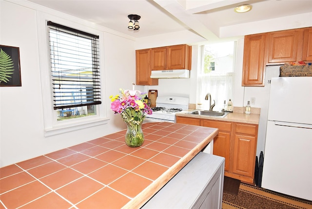 kitchen featuring white appliances, a sink, under cabinet range hood, tile countertops, and brown cabinets
