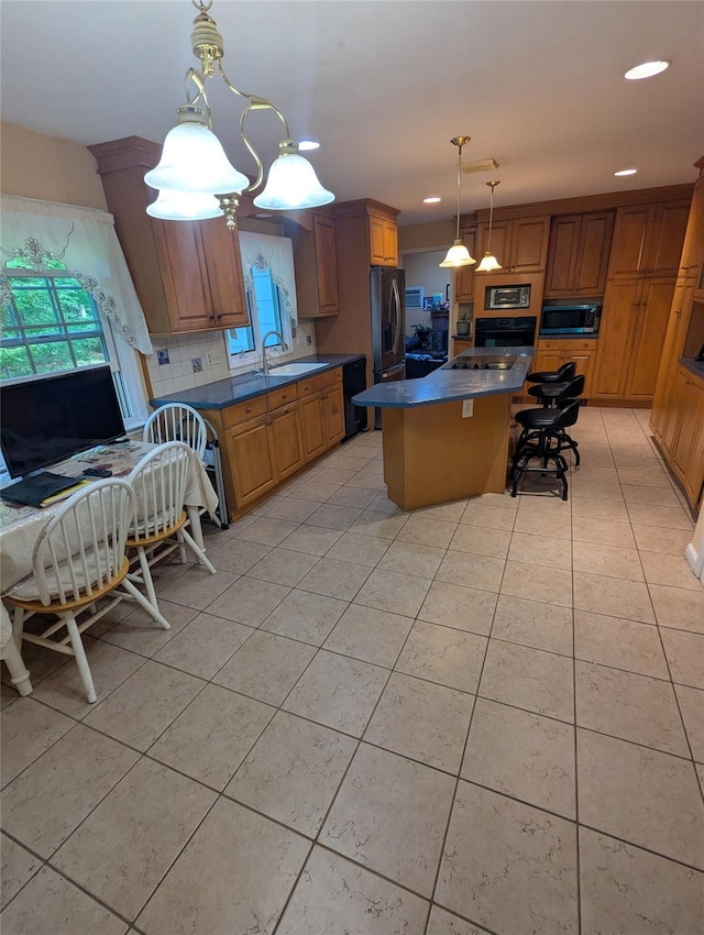 kitchen featuring stainless steel appliances, a sink, light tile patterned floors, a kitchen island, and dark countertops
