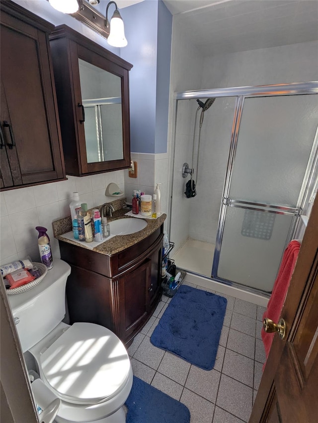 full bath with a stall shower, vanity, tile patterned flooring, toilet, and tile walls