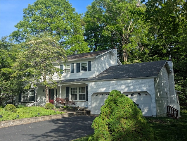view of front of house with a chimney, an attached garage, asphalt driveway, and covered porch