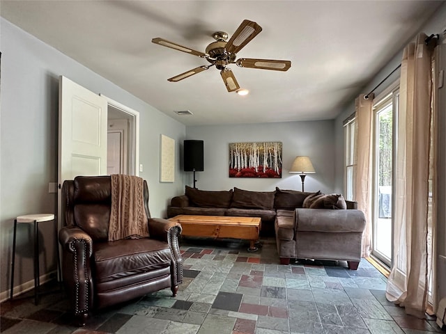 living area with stone tile flooring, ceiling fan, and baseboards
