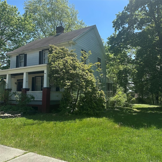 view of side of home featuring covered porch, a lawn, and a chimney