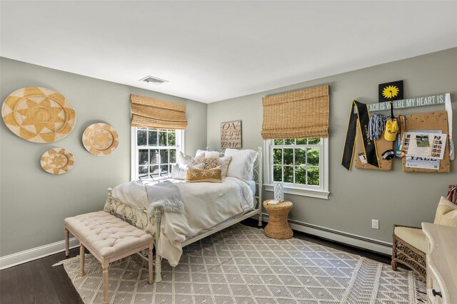 bedroom with a baseboard heating unit, wood finished floors, and baseboards