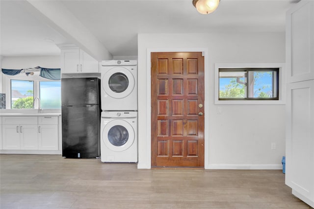 laundry area featuring stacked washer and clothes dryer, healthy amount of natural light, light wood finished floors, and baseboards