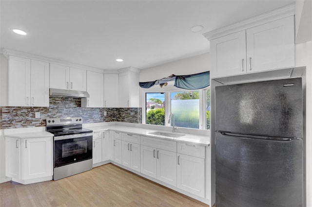 kitchen featuring freestanding refrigerator, stainless steel electric range oven, a sink, under cabinet range hood, and light countertops