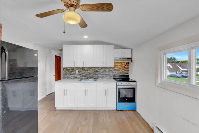 kitchen featuring freestanding refrigerator, stainless steel range with electric cooktop, a sink, under cabinet range hood, and baseboard heating