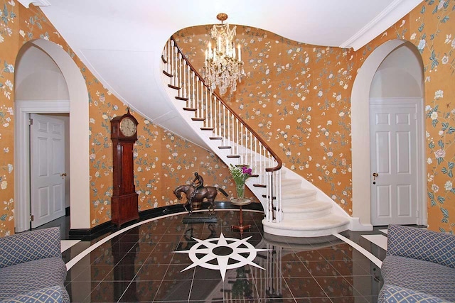 foyer featuring wallpapered walls, arched walkways, stairway, baseboards, and a chandelier