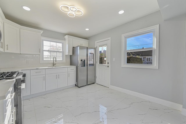 52 State St, Valley Stream, NY 11580 - kitchen with appliances with stainless steel finishes, a sink, baseboards, light marble finish floors, and white cabinets