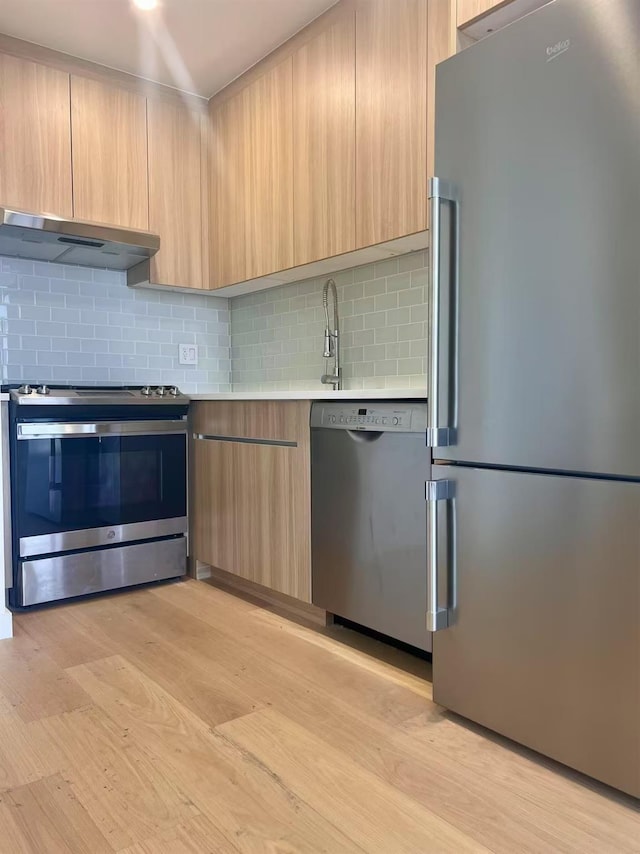 kitchen with stainless steel appliances, under cabinet range hood, modern cabinets, and light brown cabinetry