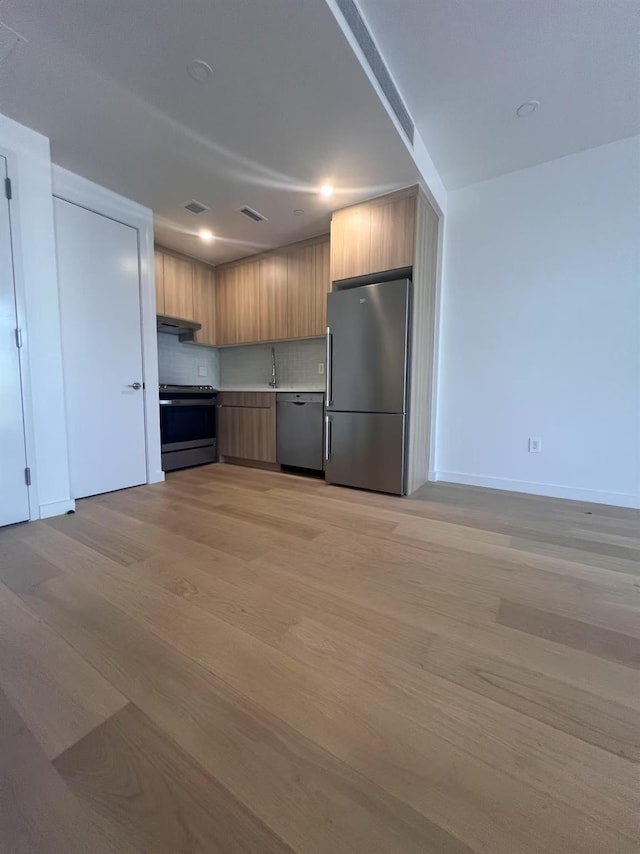 kitchen featuring stainless steel appliances, modern cabinets, light wood finished floors, decorative backsplash, and light countertops