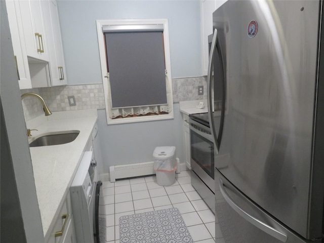 kitchen with stainless steel appliances, a sink, a baseboard radiator, light tile patterned floors, and white cabinetry