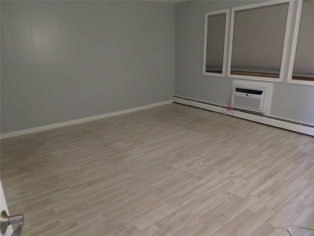 spare room with light wood-type flooring, baseboards, a baseboard heating unit, and an AC wall unit