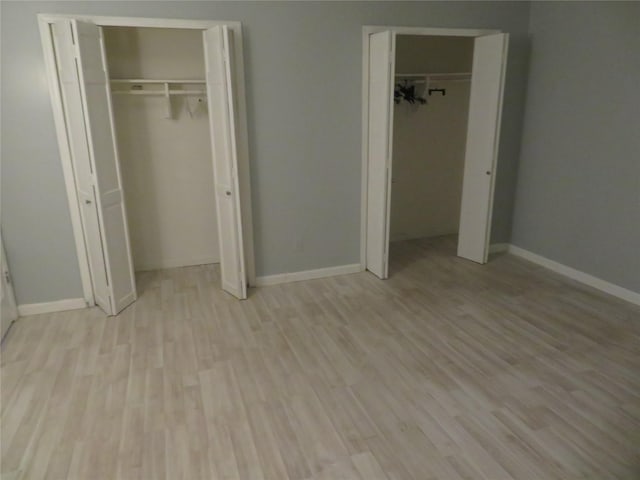 unfurnished bedroom with multiple closets, wood finished floors, and baseboards