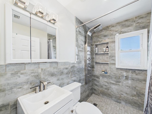 full bathroom with a tile shower, tile walls, vanity, and toilet