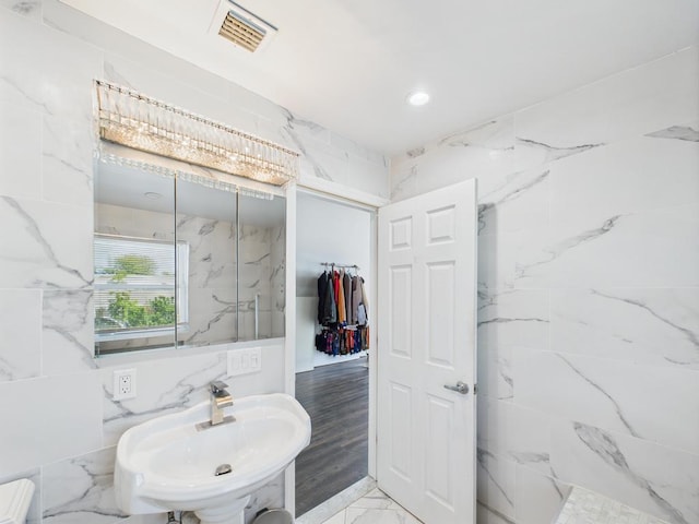 bathroom with marble finish flooring, tile walls, and a sink