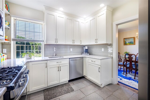 kitchen featuring stainless steel appliances, a sink, backsplash, white cabinetry, and light stone counters