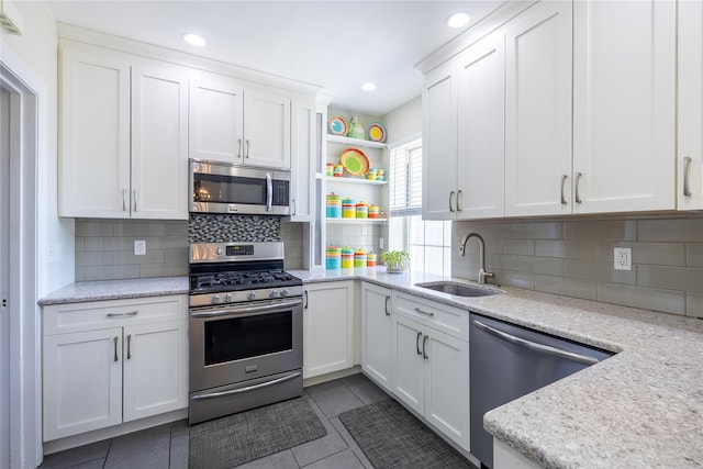 kitchen featuring appliances with stainless steel finishes, a sink, open shelves, white cabinetry, and decorative backsplash