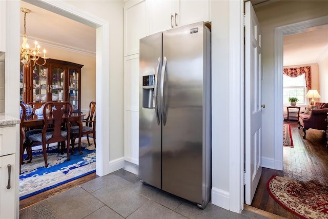kitchen featuring stainless steel refrigerator with ice dispenser, crown molding, light stone counters, a chandelier, and white cabinetry