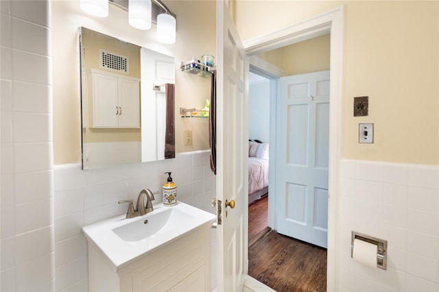 bathroom with tile walls, wood finished floors, vanity, wainscoting, and ensuite bath