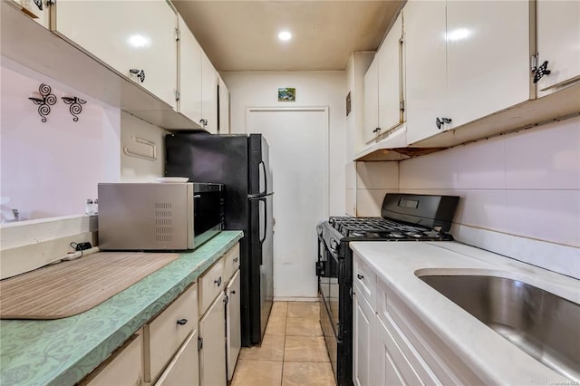 kitchen featuring black range with gas stovetop, stainless steel microwave, a sink, light tile patterned flooring, and light countertops